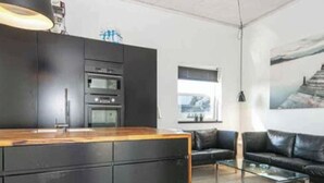A modern living room with a kitchen area, a sofa, and a coffee table. - 4 Star Holiday Home in Juelsminde (Juelsminde)