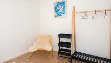 Una habitación con una silla, un estante negro, un perchero de madera y un cuadro en la pared.