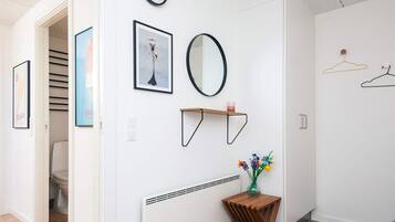 Un pasillo con un reloj, obras de arte enmarcadas, un espejo, una mesita con un florero y un radiador.