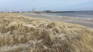 A beach with grassy dunes, a pier extending into the water, and industrial structures in the background. - 4 Person Holiday Home in Grenaa (Grenaa)