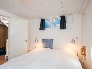 A bedroom with a bed, two bedside lamps, a window with curtains, and a door leading to another room. - 4 Person Holiday Home in Grenaa (Grenaa)