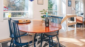 A dining area with a round wooden table, blue chairs, and a bottle of wine. - 4 Person Holiday Home in Grenaa (Grenaa)