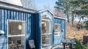 A blue house with large windows, a patio with a table and chairs, and a small garden area. - 4 Person Holiday Home in Grenaa (Grenaa)
