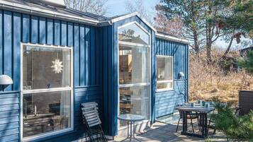 Uma casa azul com janelas amplas, um pátio com mesa e cadeiras, e um pequeno jardim.
