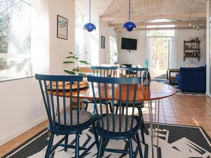 A dining area with a wooden table and blue chairs, a television mounted on the wall, and a view of the outdoors through a large window. - 4 Person Holiday Home in Grenaa (Grenaa)