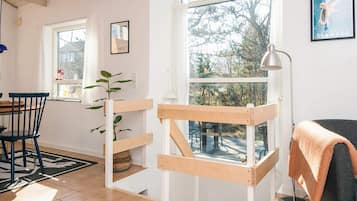 Una habitación con una cama litera de madera, una mesa de comedor con sillas, una lámpara y un gran ventanal con vistas a árboles.