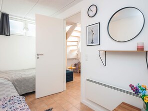 A room with a bed, a door leading to another room, a wall-mounted clock, a mirror, and a shelf with a vase of flowers. - 4 Person Holiday Home in Grenaa (Grenaa)