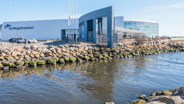 A modern building with a large sign reading 'Kattegatcentrum,' a parking area, and a rocky shoreline. - 4 Person Holiday Home in Grenaa (Grenaa)