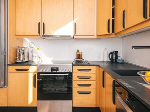 A modern kitchen with wooden cabinets, a stainless steel stove, and a coffee machine. - 4 Person Holiday Home in Grenaa (Grenaa)