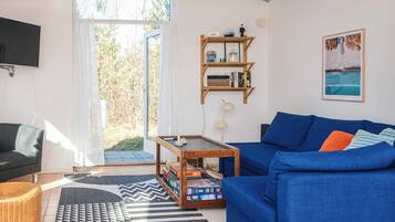 Una sala de estar con un sofá azul, una mesa de centro de madera, una estantería y un televisor montado en la pared.