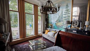 Een slaapkamer met een groot raam, een kroonluchter, een bank met kussens, een glazen salontafel en een bed.
