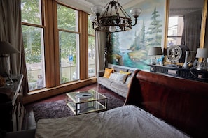 A bedroom with a large window, a chandelier, a sofa with cushions, a glass coffee table, and a bed. - Redlightdistrict Chinacitycentre Palace (Amsterdam)