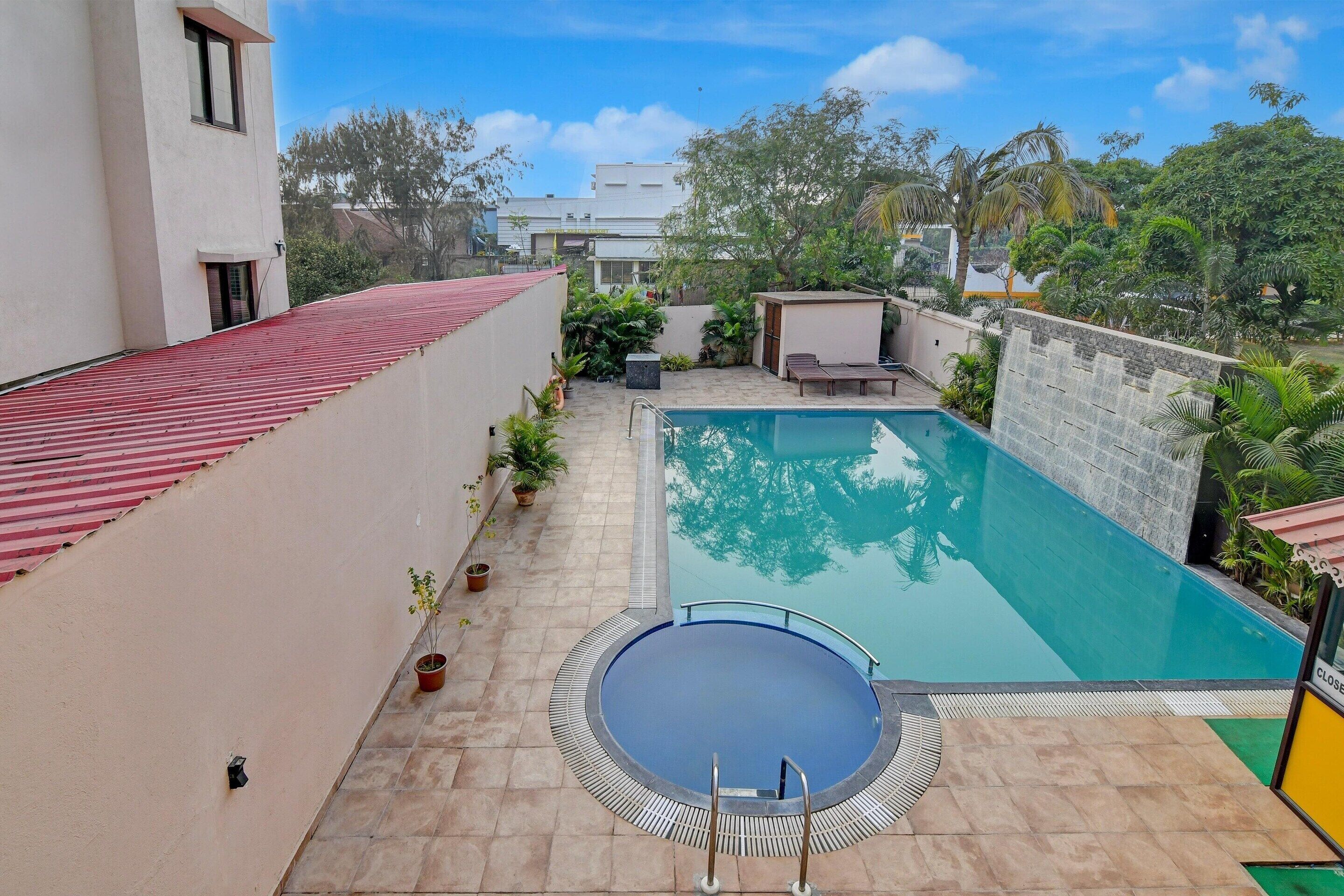 A swimming pool with a red roofed area, a small covered seating area, and a stone wall.