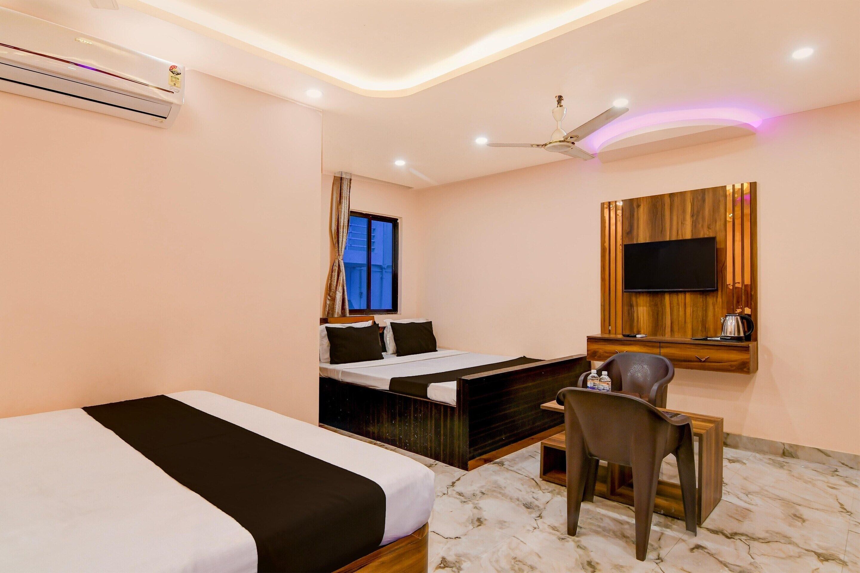 A hotel room with a bed, a desk, a chair, a TV mounted on the wall, and an air conditioning unit.