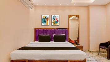 A modern hotel room with a wooden bed frame, a purple headboard, two black pillows, a white bedspread, a wooden nightstand with a phone, and a mirror.