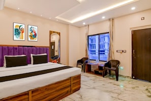 Habitación de hotel con cama, escritorio, silla, ventana y cuadros en la pared.