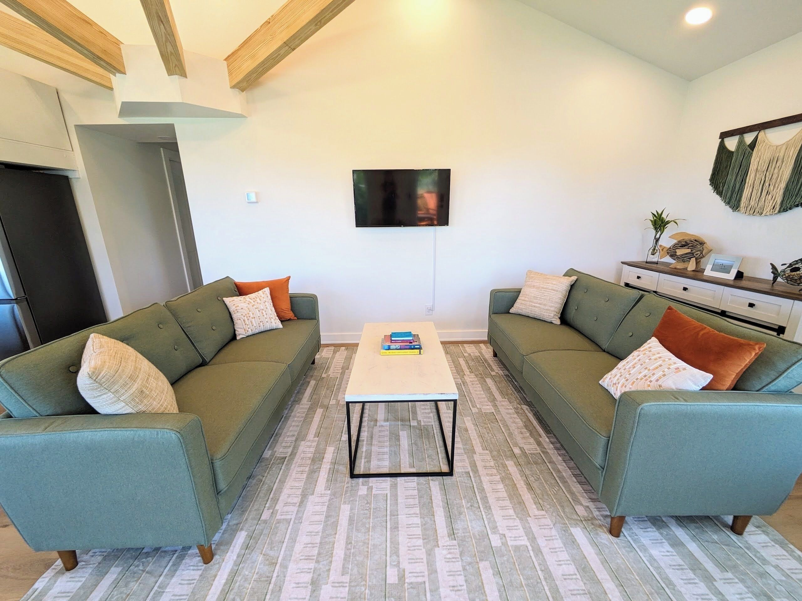 A living room with two green sofas, a coffee table, and a TV mounted on the wall.