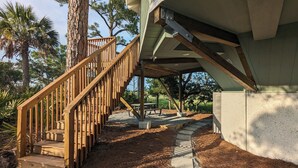 Una scala in legno conduce a una zona esterna coperta, con pavimento in cemento e vista su alberi e prato.