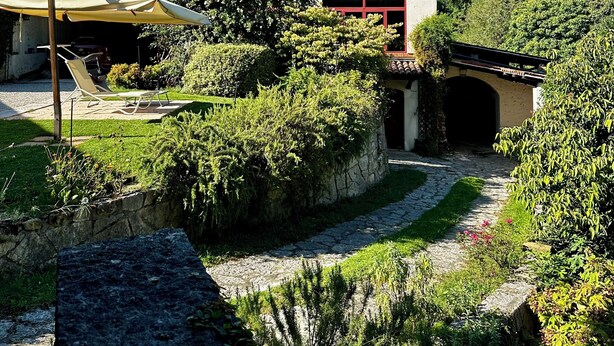 Una casa con jardín, un espacio de estar al aire libre cubierto y un sendero de piedra que lleva a un túnel.