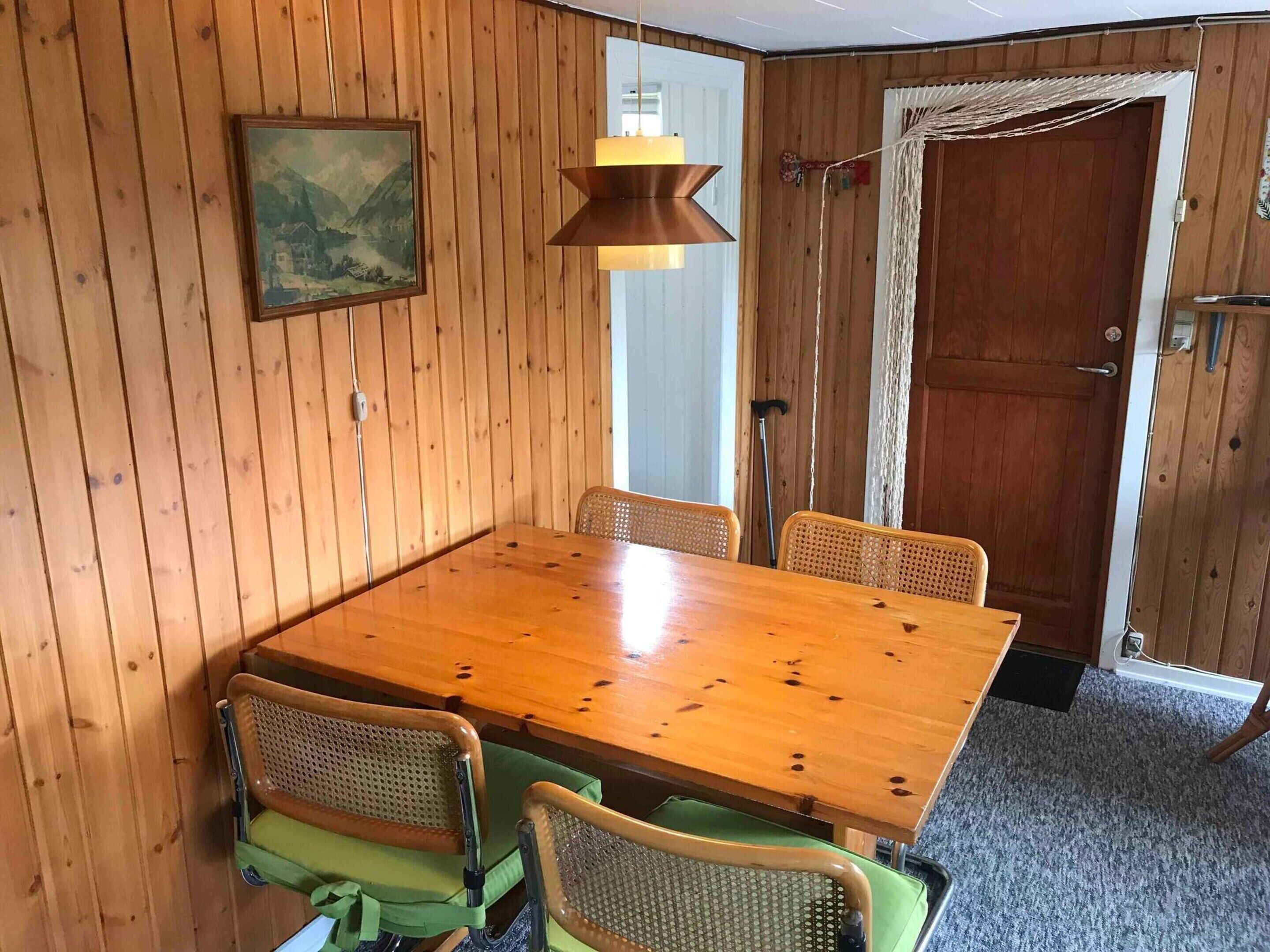 A wooden-paneled room with a wooden dining table and four wicker chairs.