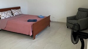 Ein Schlafzimmer mit Bett, Stuhl, Standventilator und Deckenleuchte.
