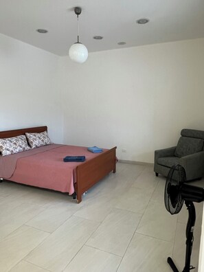 A bedroom with a bed, a chair, a standing fan, and a ceiling light. - Two-room apartment cervia mirabilandia zoo safari (Fosso Ghiaia)