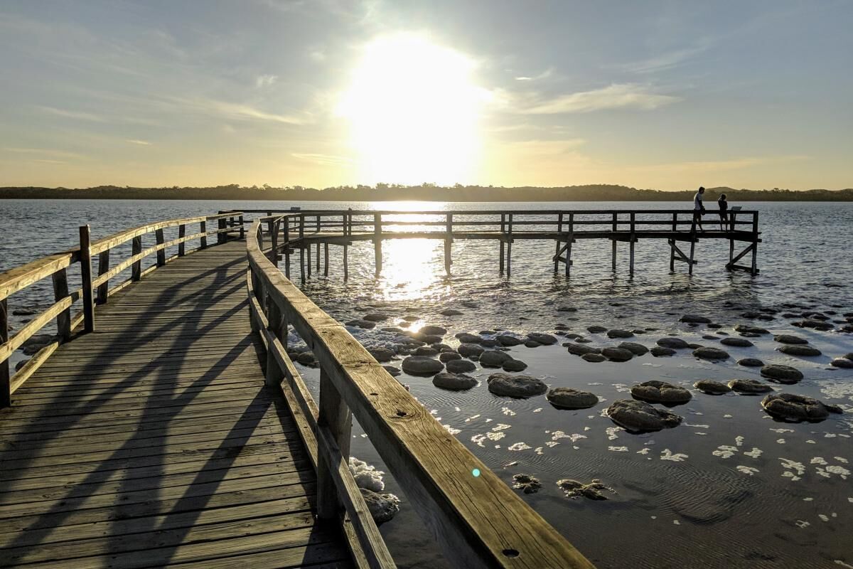 A wooden pier extending into calm water with a sunset in the background.