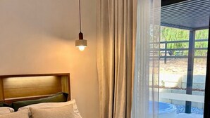 A bed with a headboard, a hanging light, and a view of an outdoor area through a window. - Brand New 2x2 Escape | Relax & Unwind (Herron)