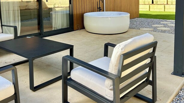A covered outdoor seating area with a hot tub, tables, and chairs. - Brand New 2x2 Escape | Relax & Unwind (Herron)