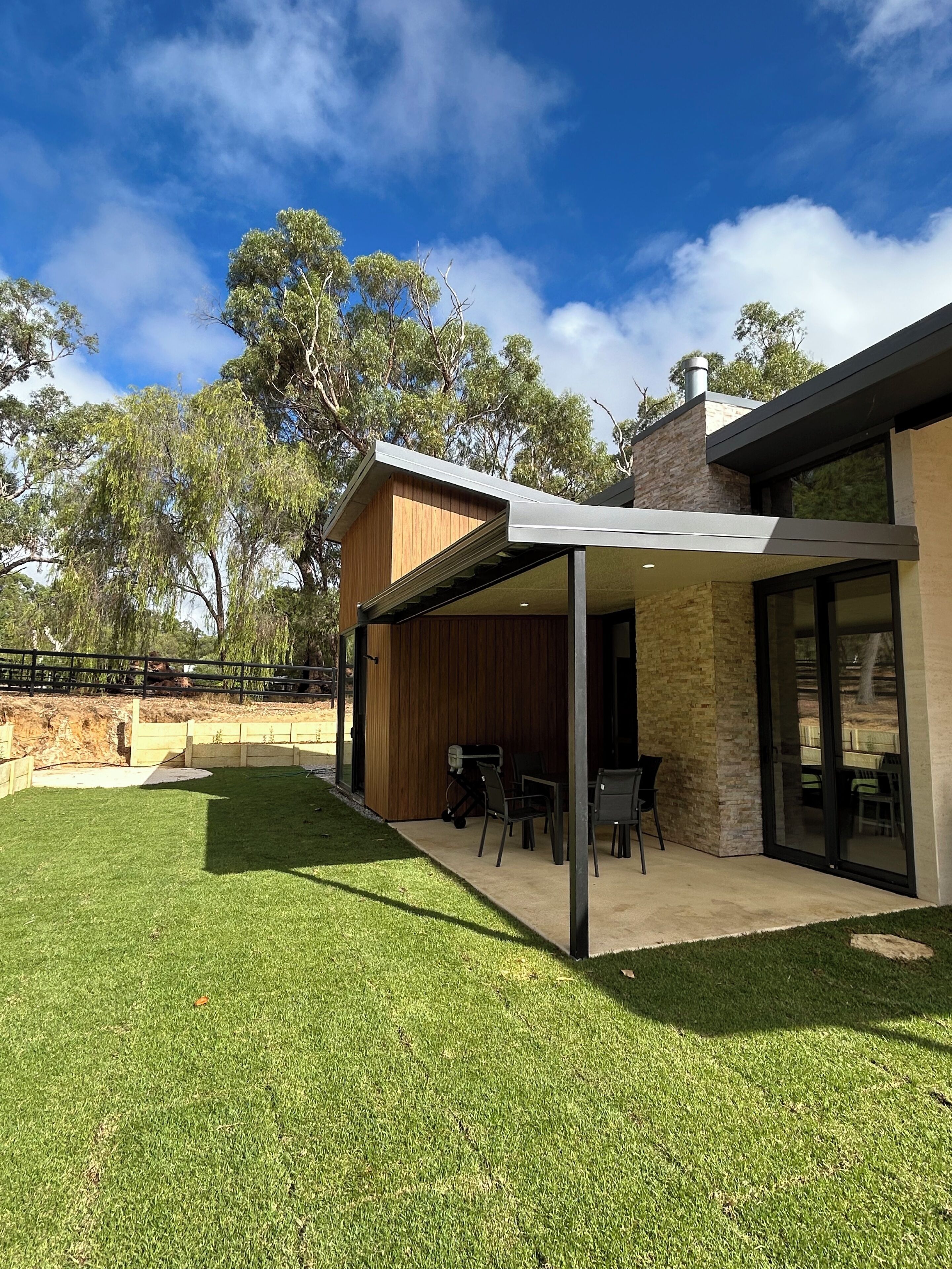 Une maison moderne dotée d’un patio couvert, d’un espace salon extérieur et d’une pelouse bien entretenue.