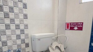 Ein kleines Badezimmer mit Toilette, einem roten Eimer und einem Schild in einer Fremdsprache.