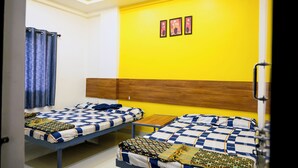 Ein Zimmer mit zwei Betten, einem Holzkopfteil, einem kleinen Tisch und einer gelben Wand mit drei gerahmten Bildern.