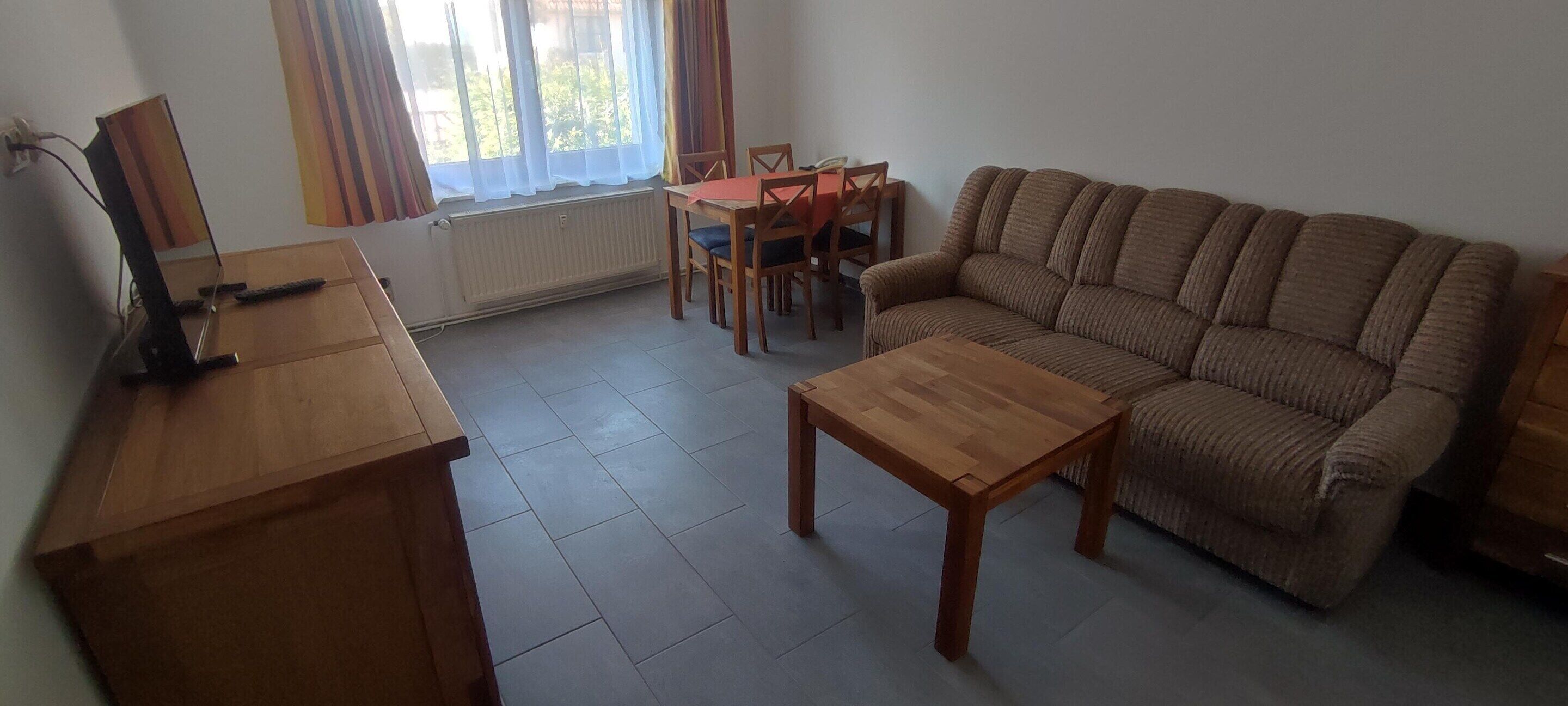A living room with a sofa, a wooden coffee table, a dining table with chairs, and a TV.