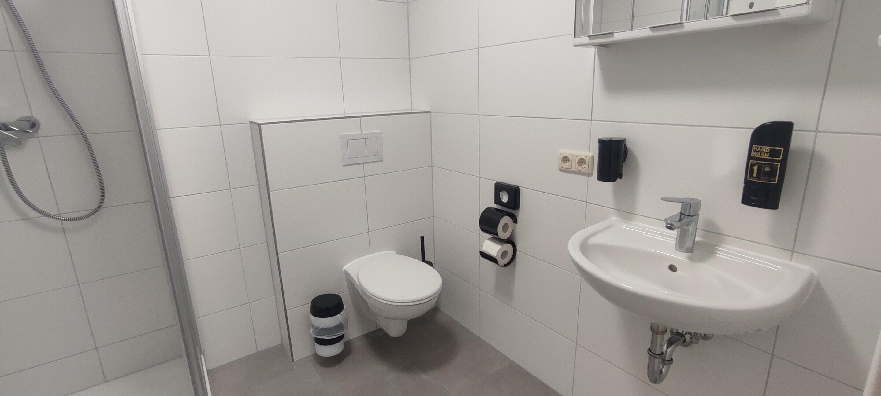 A bathroom with a toilet, sink, hand dryer, and a shower.