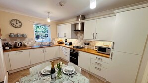 A modern kitchen with white cabinets, a wooden countertop, a built-in microwave, and a dining area set for four with a floral tablecloth. - Tranquil retreat in idyllic Wooler, Northumberland National Park, pet friendly (Wooler)
