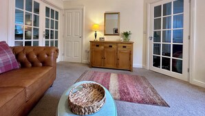 A living room with a brown leather sofa, a wooden cabinet, a lamp, and a mirror on the wall. - Tranquil retreat in idyllic Wooler, Northumberland National Park, pet friendly (Wooler)