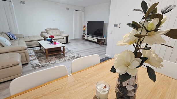 A living room with a sofa, a coffee table, a TV, and a vase with flowers. - Spacious 3‑Bedroom | Family & Work Stay | Near Campbelltown Hospital (Airds)