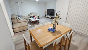 A living room with a sofa, a coffee table, a TV, and a dining table with chairs. - Spacious 3‑Bedroom | Family & Work Stay | Near Campbelltown Hospital (Airds)