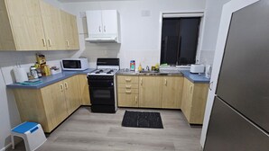A compact kitchen with a gas stove, microwave, sink, and wooden cabinets. - Spacious 3‑Bedroom | Family & Work Stay | Near Campbelltown Hospital (Airds)