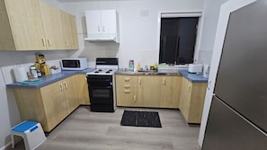 A compact kitchen with a gas stove, microwave, sink, and wooden cabinets. - Spacious 3BR Home for Family & Work Stays Near Campbelltown | Parking Fast WiFi (Airds)