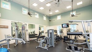 Un gimnasio con ventiladores de techo, equipo de ejercicio y una pantalla de televisión.