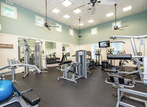 A gym with ceiling fans, exercise equipment, and a TV screen. - Oceanfront beauty in Cinnamon Beach - 523! (Palm Coast)