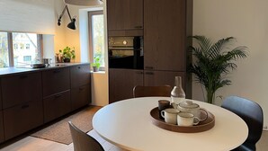 A modern kitchen with dark wood cabinets, a round dining table with a tray of cups and a teapot, and a potted plant. - Stylish Apartment in Bree Centre (Bree)