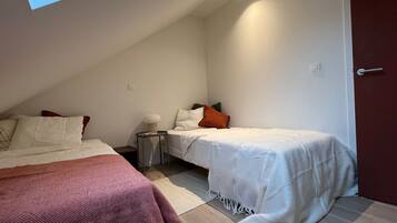 A bedroom with two beds, a bedside table, a lamp, and a door.
