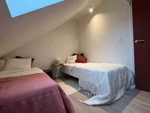 A bedroom with two beds, a bedside table, a lamp, and a door. - Stylish Apartment in Bree Centre (Bree)