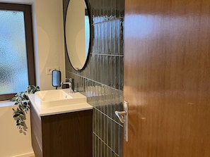 A bathroom with a white sink, a mirror, and a wooden door. - Stylish Apartment in Bree Centre (Bree)