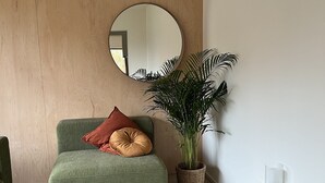 A green sofa with two pillows, a large potted plant, a round mirror, and a small table with a glass object. - Stylish Apartment in Bree Centre (Bree)