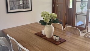 A dining area with a wooden table, white chairs, a vase with flowers, and a framed picture on the wall.