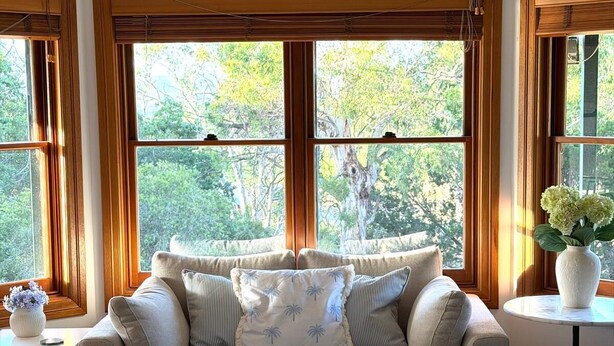 A cozy living room with a beige sofa, a white coffee table, and a view of trees through large windows.
