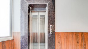 Um elevador com mostrador digital, parede de painel de madeira e porta de vidro.